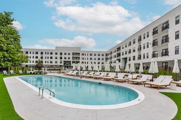 A large swimming pool surrounded by lounge chairs and umbrellas in front of a building.