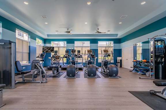 A spacious gym with a variety of equipment and a ceiling fan.