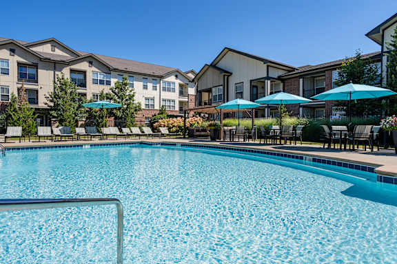 A swimming pool surrounded by apartment buildings and lounge chairs.