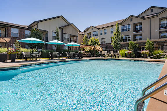 A swimming pool surrounded by apartment buildings and umbrella-covered lounge chairs.