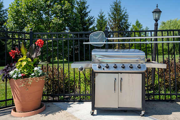 A small outdoor stove is on a patio next to a potted plant.