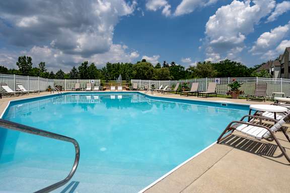 A large outdoor swimming pool surrounded by a metal fence and lounge chairs.