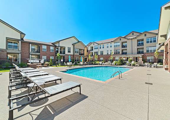 A swimming pool surrounded by sun loungers in front of apartment buildings.