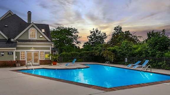 A swimming pool in front of a house with a sunset in the background.