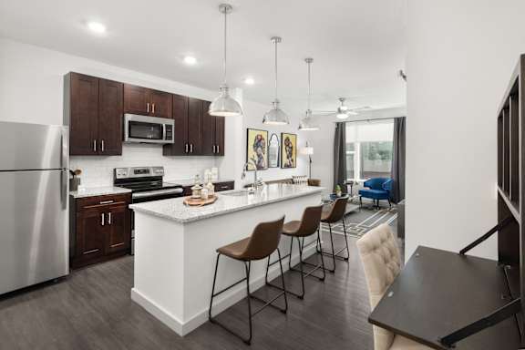A modern kitchen with a white island and brown chairs.