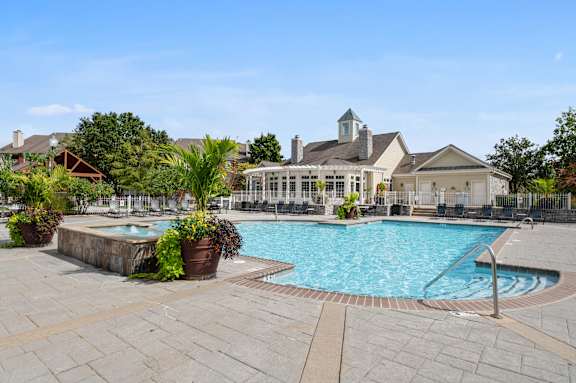 A large outdoor swimming pool surrounded by a stone patio and a building in the background.