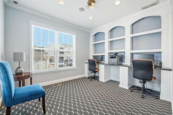 A room with a blue chair in front of a desk with a lamp on it.