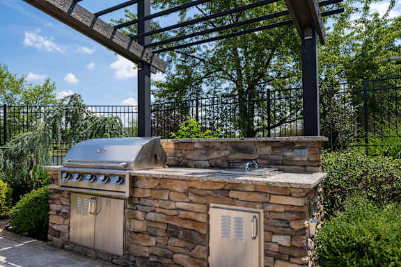 A stone outdoor kitchen with a grill and a pergola.