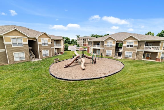 A playground with a slide and a merry-go-round is surrounded by apartment buildings.