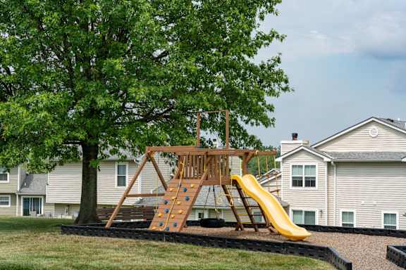 A wooden swing set with a yellow slide is in the foreground of a residential area.