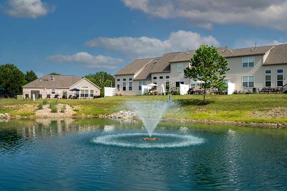 A fountain in the middle of a pond in front of a row of houses.