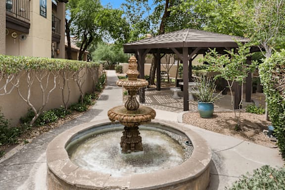 A fountain in the middle of a courtyard with a gazebo in the background.