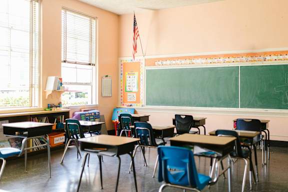 a classroom with desks and chairs and a bulletin board on the wall
