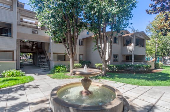 A fountain in the middle of a courtyard surrounded by trees and buildings at The Woods Apartments, San Jose