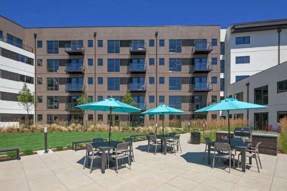 A patio with tables and chairs and umbrellas in front of a building.