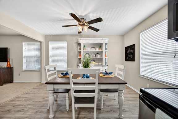 A dining room with a table set for two and a ceiling fan.