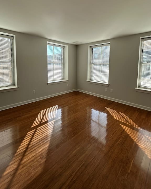 A room with wooden floors and three windows letting in sunlight.