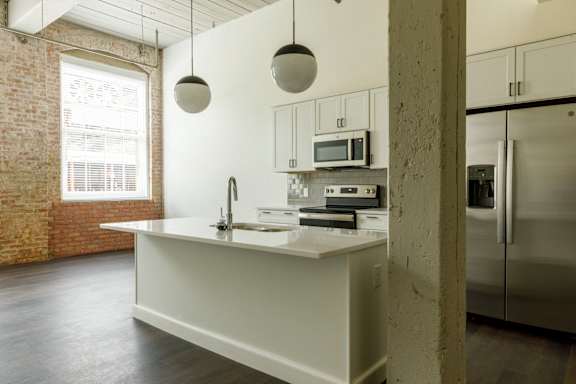 A kitchen with a white counter and a brick wall.