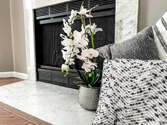 A vase with white flowers sits in front of a fireplace.