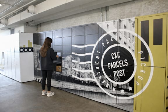A woman is standing in front of a mural with the words "Exc Parcels Post" written on it.