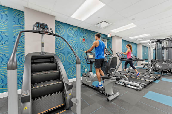 A man and a woman are exercising on treadmills in a gym.