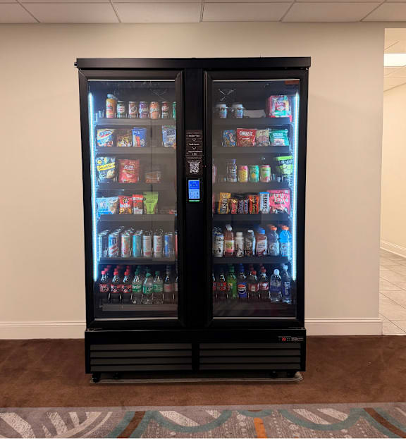 A black double sided fridge with drinks and snacks on both sides.