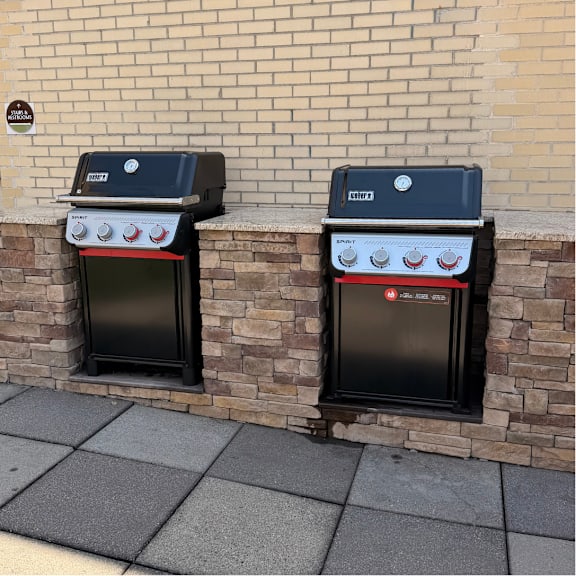 Two black Weber grills are on a brick wall.