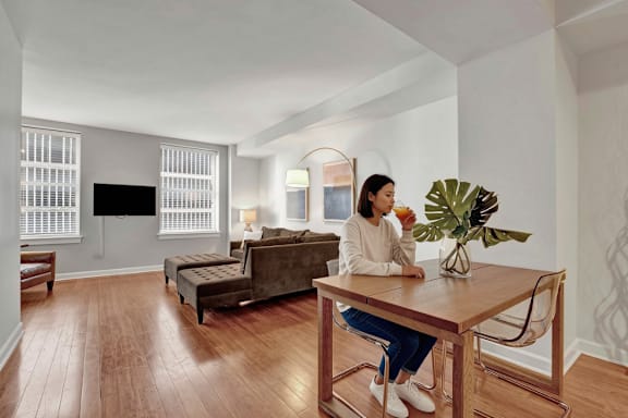 A woman is sitting at a wooden table in a room with a brown couch and a TV.