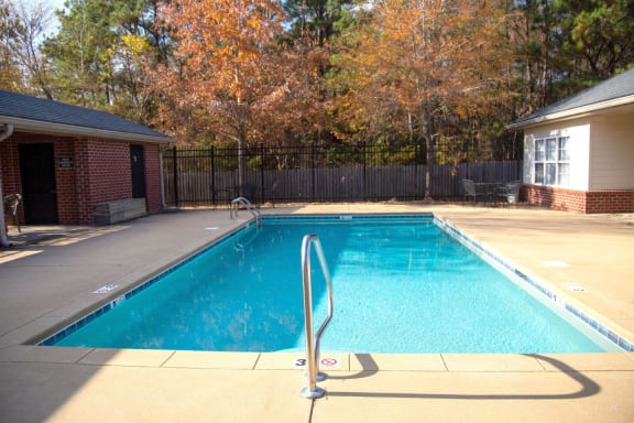 a swimming pool in front of a house with a black fence