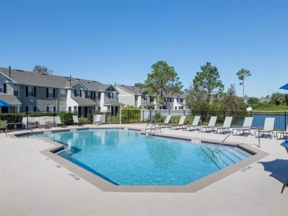 a resort style pool with chaise lounge chairs and apartment buildings in the background