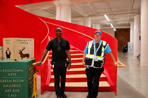 Two security guards standing in front of a red staircase.