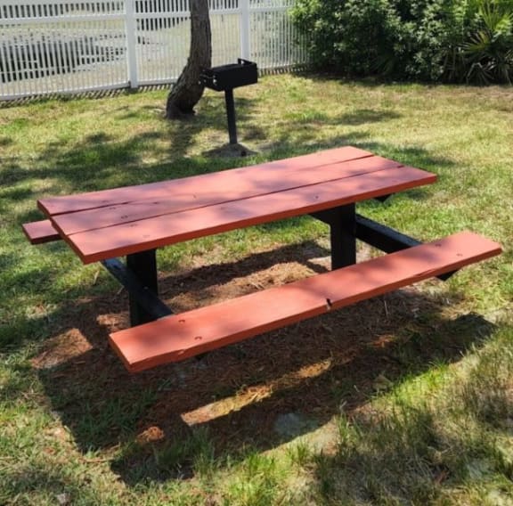 a picnic table in a grassy area with a grill in the background
