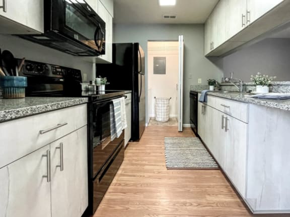 a kitchen with white cabinets and black appliances and a wood floor