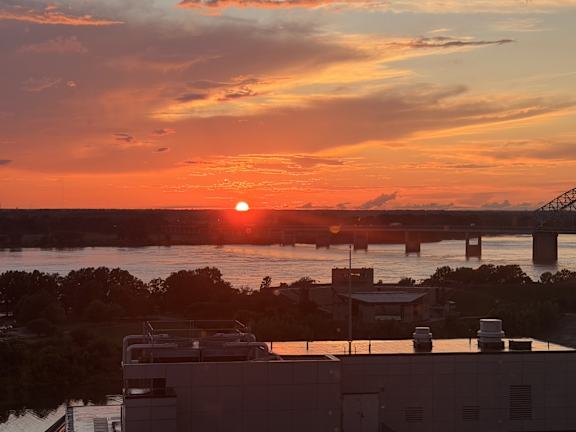 The sun is setting behind a bridge over a body of water.