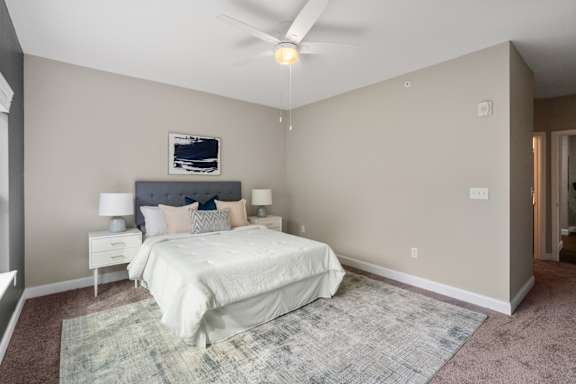 A bedroom with a bed, nightstand, and ceiling fan.