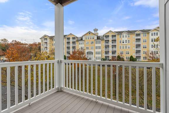 A balcony with a white railing overlooks apartment buildings.