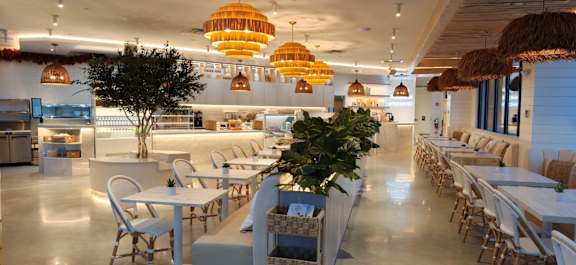 A restaurant with white tables and chairs and hanging lights.