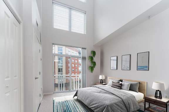 A bedroom with a large bed and a view of a building outside the window.