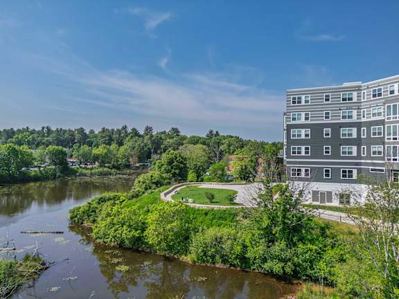 A modern building is situated by a body of water with a green area in front of it.
