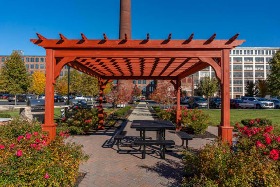 a picnic table under a wooden pavilion on a brick sidewalk