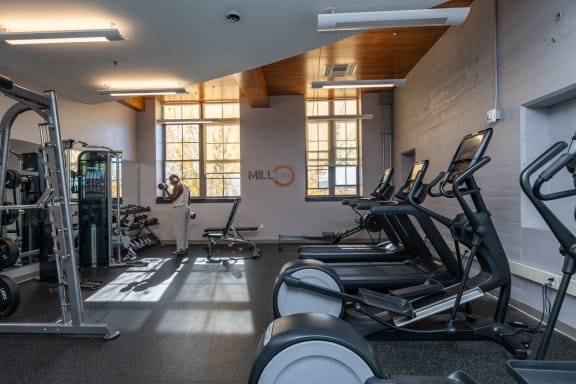a gym with cardio equipment and a person by the window