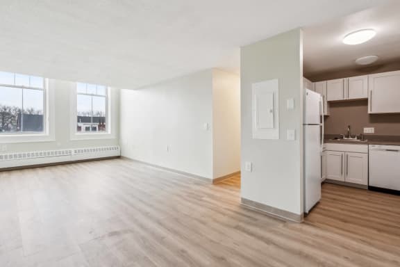 the living room and kitchen of an empty apartment with white walls and wood floors at Chapman House, E. Boston