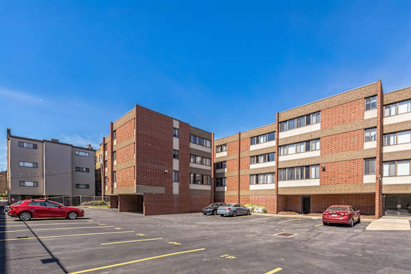 A parking lot in front of a brick apartment building with cars parked.