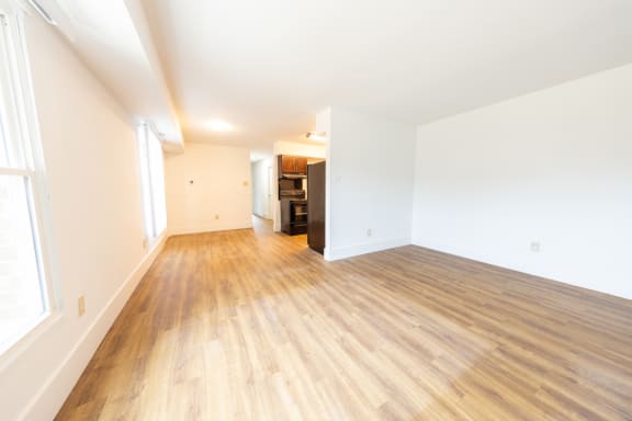 an empty living room with hardwood floors and a kitchen in the background