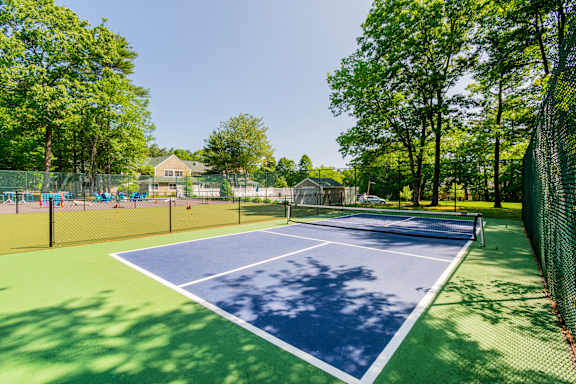 A Pickleball court surrounded by a fence and trees atat Mariner's Hill Apartments, Massachusetts.