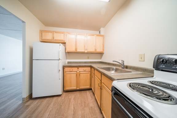A kitchen with a white refrigerator, wooden cabinets, and a white stove top oven at Highpoint Towers Apartments, Erie, PA