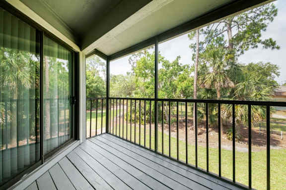 A balcony with a black railing and sliding glass doors overlooking a grassy area at Fisherman's Landing Apartments, Ormond Beach, Florida