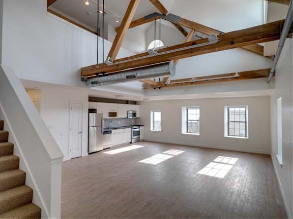 an open living room with a kitchen and exposed beams in the ceiling at Ames Shovel Works Apartments, Massachusetts, 02356