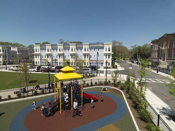 A playground with a yellow canopy and red slide is surrounded by a fence and apartment buildings at The Anne M. Lynch Homes at Old Colony, South Boston, MA