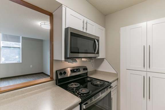 A kitchen with a black stove top oven and white cabinets at Mill House Apartments, Greenfield, MA, 01301